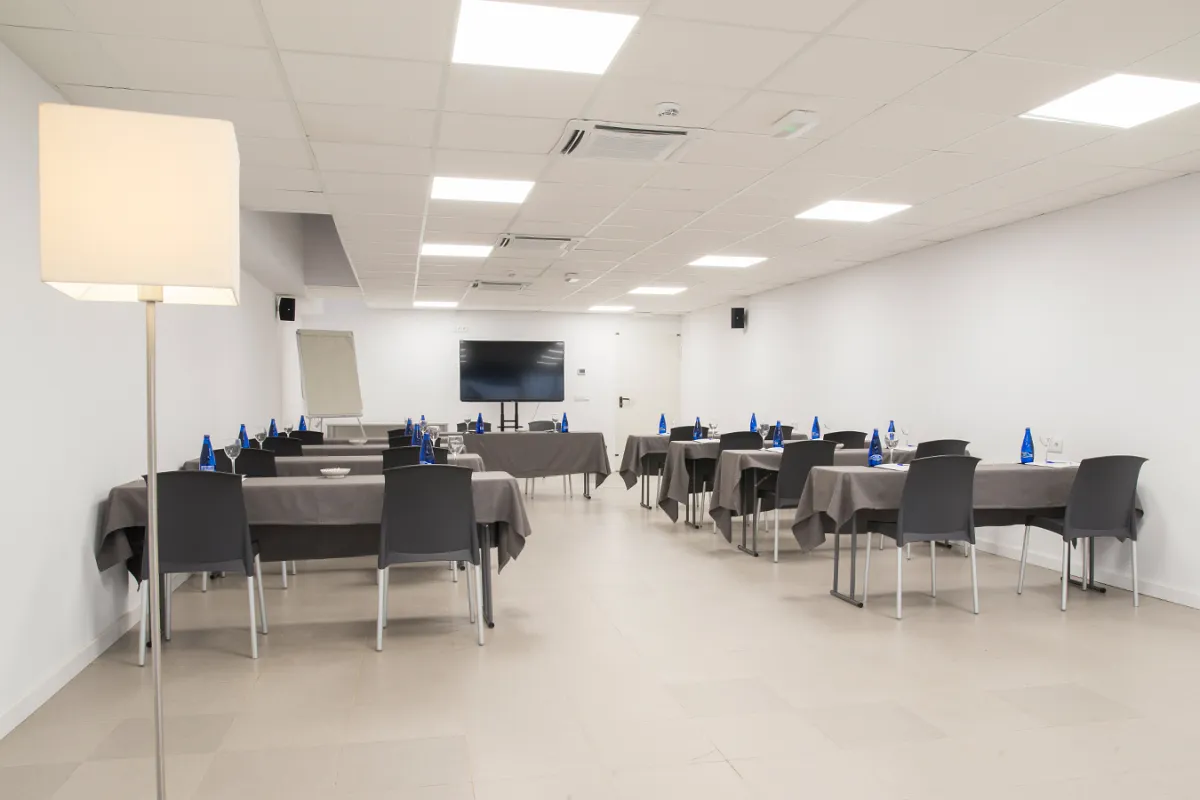 Sala de reuniones con mesas, sillas y una pantalla al fondo.