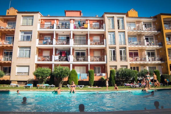 Complejo hotelero con piscina y personas nadando frente a apartamentos.