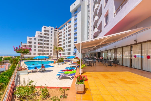 Vista de piscina y terraza con edificios de hotel y cielo azul.