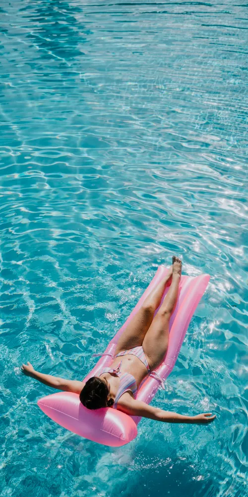 Mujer nadando sobre flotador rosa en el agua turquesa.