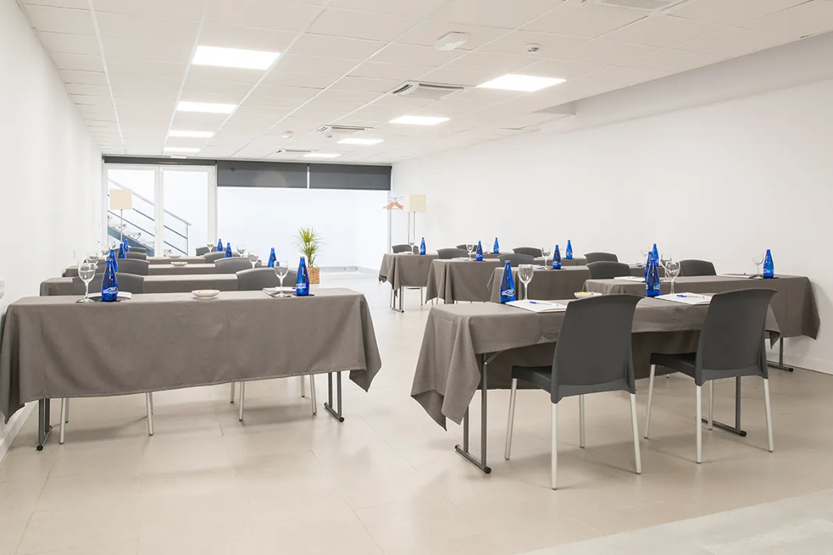 Sala de reuniones con mesas vestidas y sillas preparadas para un evento.