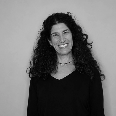 Smiling woman with curly dark hair against a light background, black top