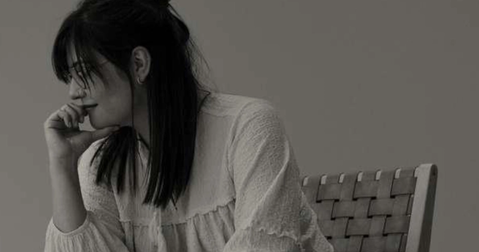 Young woman with black hair covering her mouth, looking away beside a chair