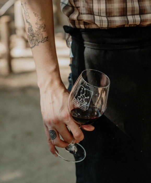 Person with floral tattoo holding a glass of red wine outdoors