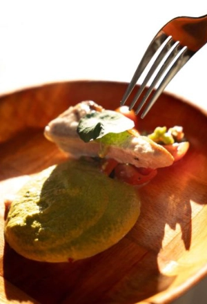 Fork eating green-topped dish with meat and vegetables on a wooden plate