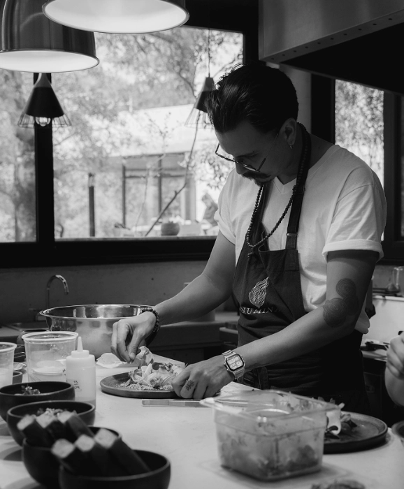 Chef in apron preparing food at a kitchen table in black-and-white.