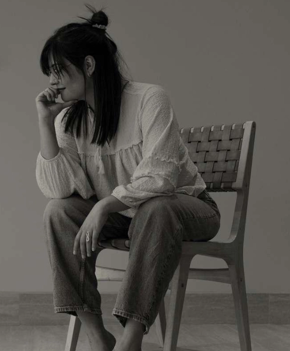 Young woman sitting on a chair, gazing down in grayscale.