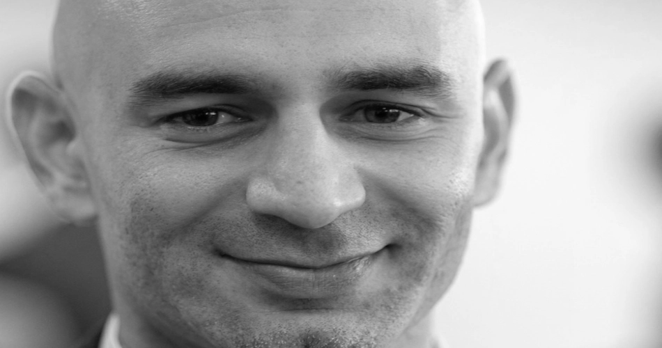 Black-and-white close-up portrait of a smiling bald man with eyes open