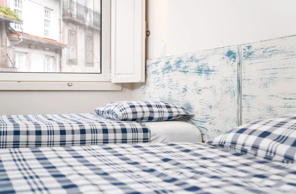 Cama con ropa de cama azul y blanca junto a ventana y pared azul con mapa
