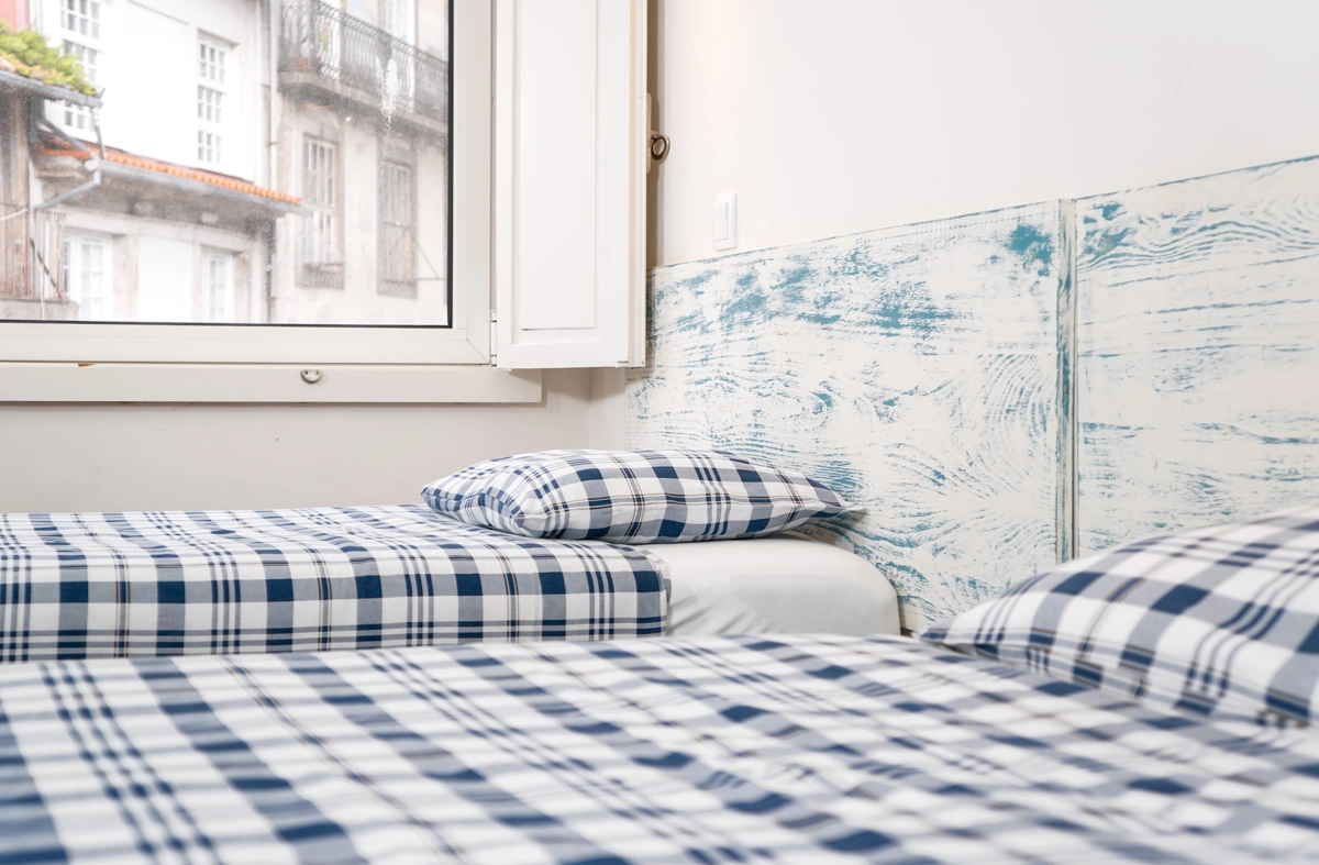 Cama con ropa de cama azul y blanca junto a ventana y pared azul con mapa