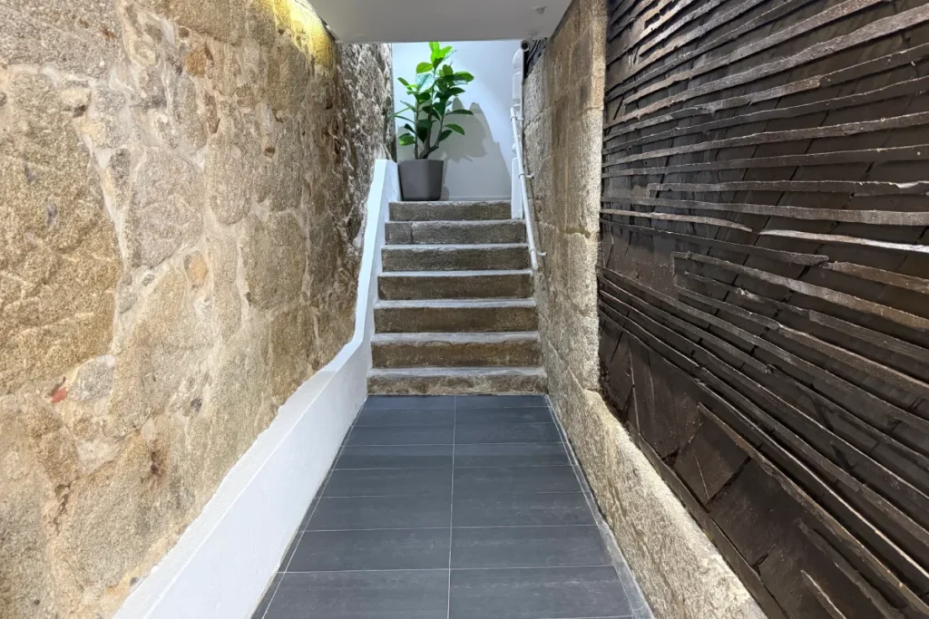 Pasillo estrecho con escaleras, paredes de piedra y puerta de madera oscura