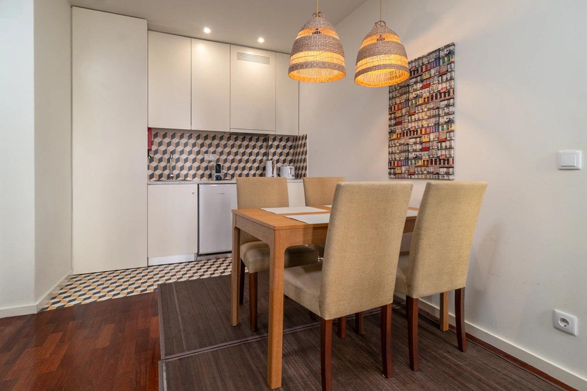 Comedor moderno con mesa de madera y sillas beige, cocina al fondo y l&aacute;mparas colgantes
