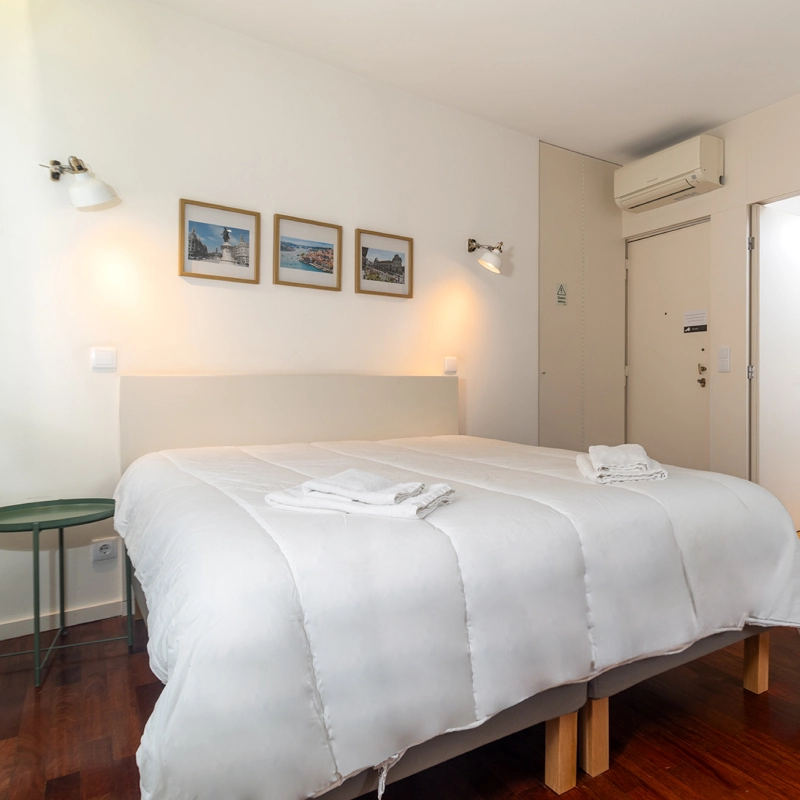 Dormitorio moderno con cama blanca, cuadros y puerta de entrada con aire acondicionado