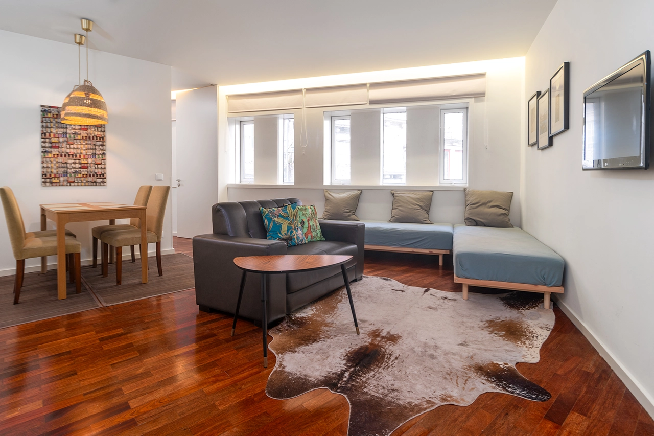 Sala luminosa con sof&aacute; gris, mesa y alfombra, comedor y cuadros en pared