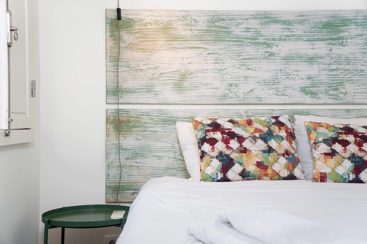 Dormitorio con cama blanca y cojines de colores, pared con madera verde y silla verde