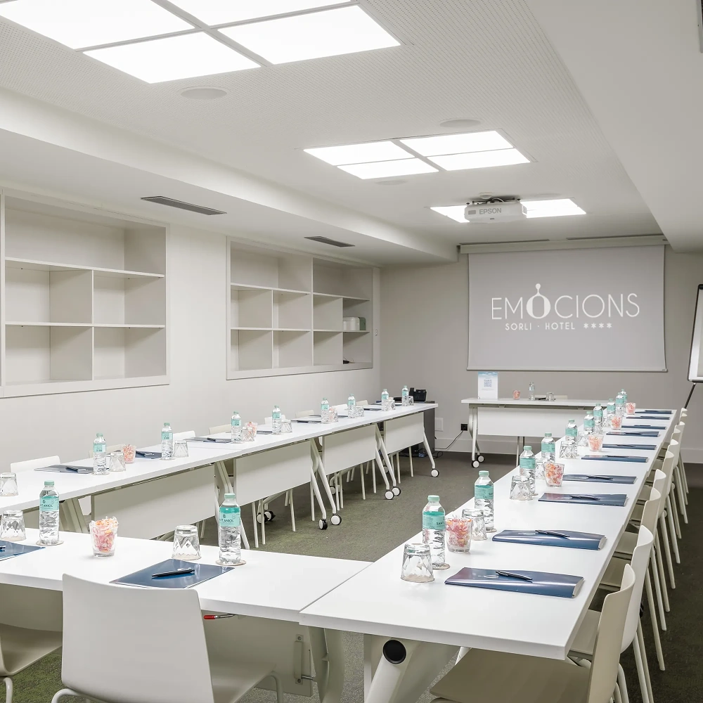 Sala de reunions amb taula i cadires, projector i pantalla &ldquo;EMOCIONS&rdquo; d&rsquo;hotel