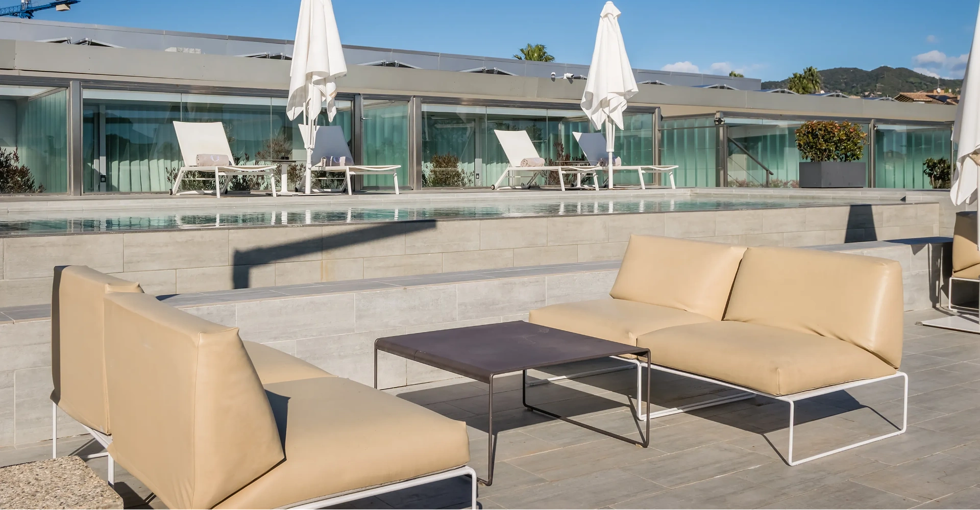 Terrassa moderna amb piscina, gandules i para-sols blancs, vistes a les muntanyes.
