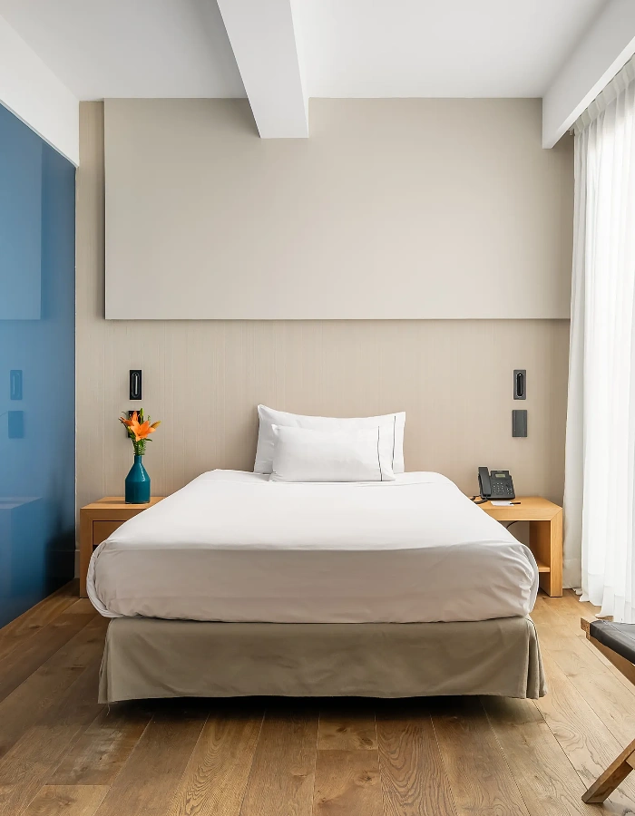 Habitaci&oacute; hotelera moderna amb llit doble, dos coixins i llum de taula.