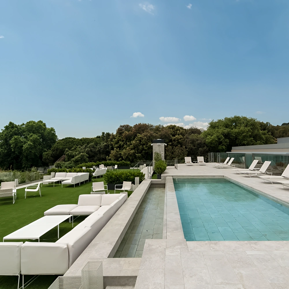 Terraza con piscina y tumbonas blancas, rodeada de jardines y colinas verdes