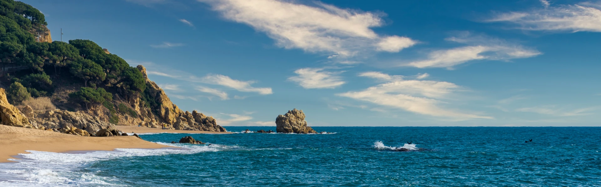 Playa con rocas y acantilados, oleaje y cielo azul con nubes sobre el mar