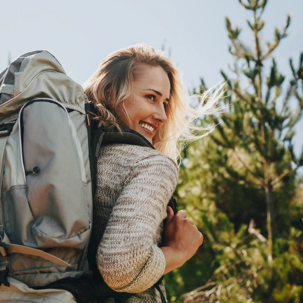 Mujer sonriente con mochila abrazando a un compa&ntilde;ero en un sendero al aire libre