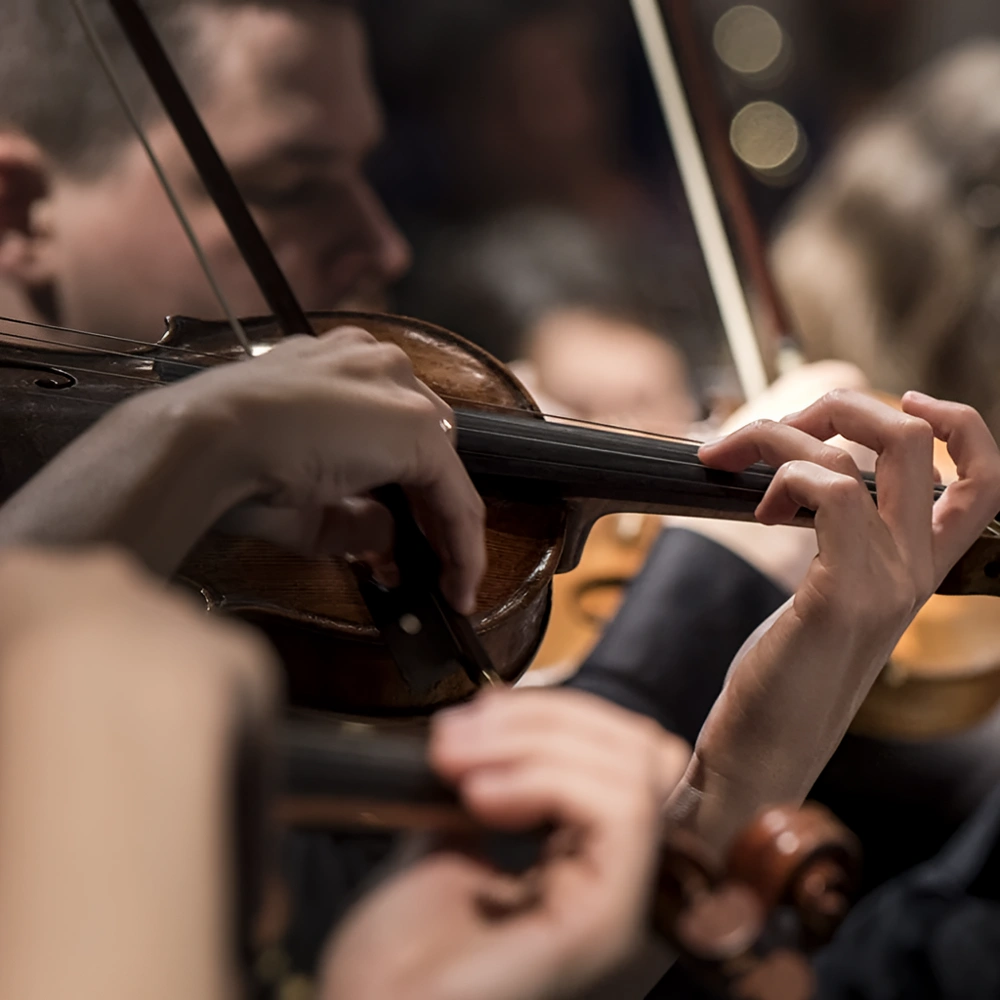 Manos afinando un violonchelo en un concierto, con el arco cerca del puente