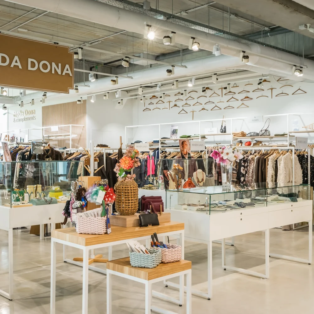 Tienda de ropa con maniqu&iacute;es, mesas y accesorios; letrero &ldquo;Moda Dona&rdquo;