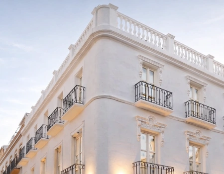Fachada de edificio blanco con balcones y balc&oacute;n central en la azotea.