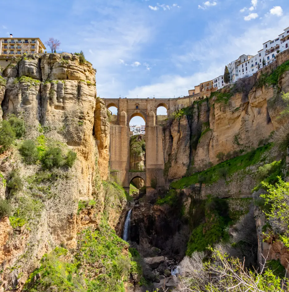 Puente de piedra y acueducto sobre ca&ntilde;&oacute;n con casas al borde, en cielo azul
