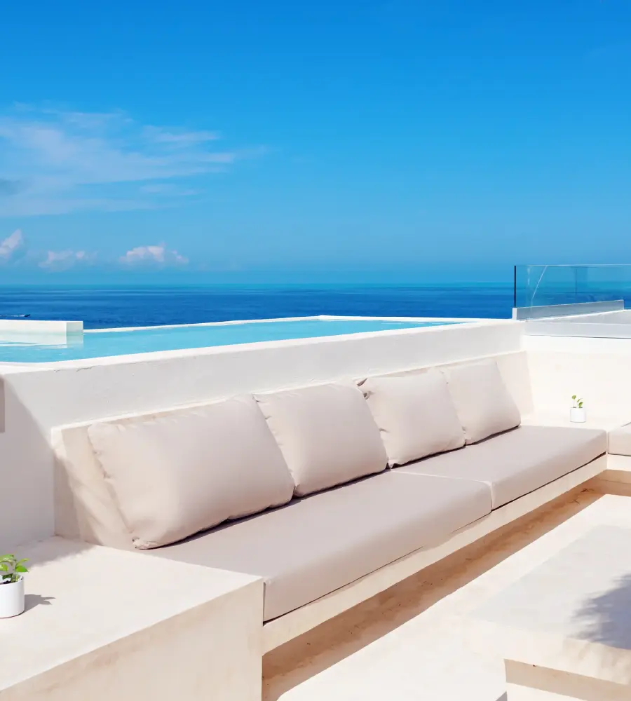 Terraza blanca con cojines y vista al mar azul desde un balc&oacute;n moderno
