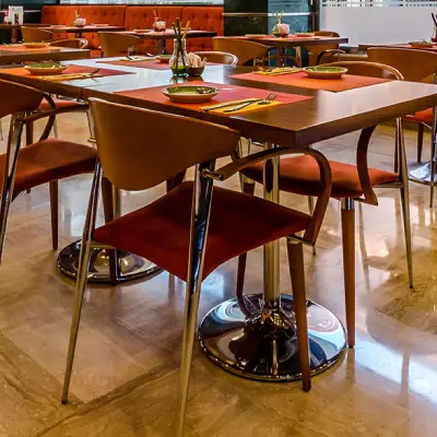 Sal&oacute;n de restaurante con mesas y sillas de metal, manteles rojos y dorados.