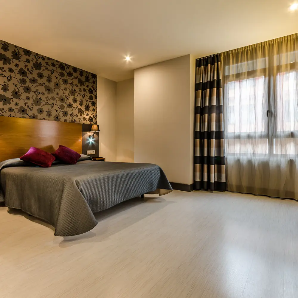 Dormitorio moderno con cama, cortinas y l&aacute;mpara encendida.