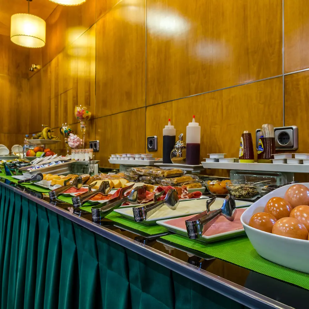 Buffet con platos de comida y bol de salchichas en sala iluminada con l&aacute;mparas