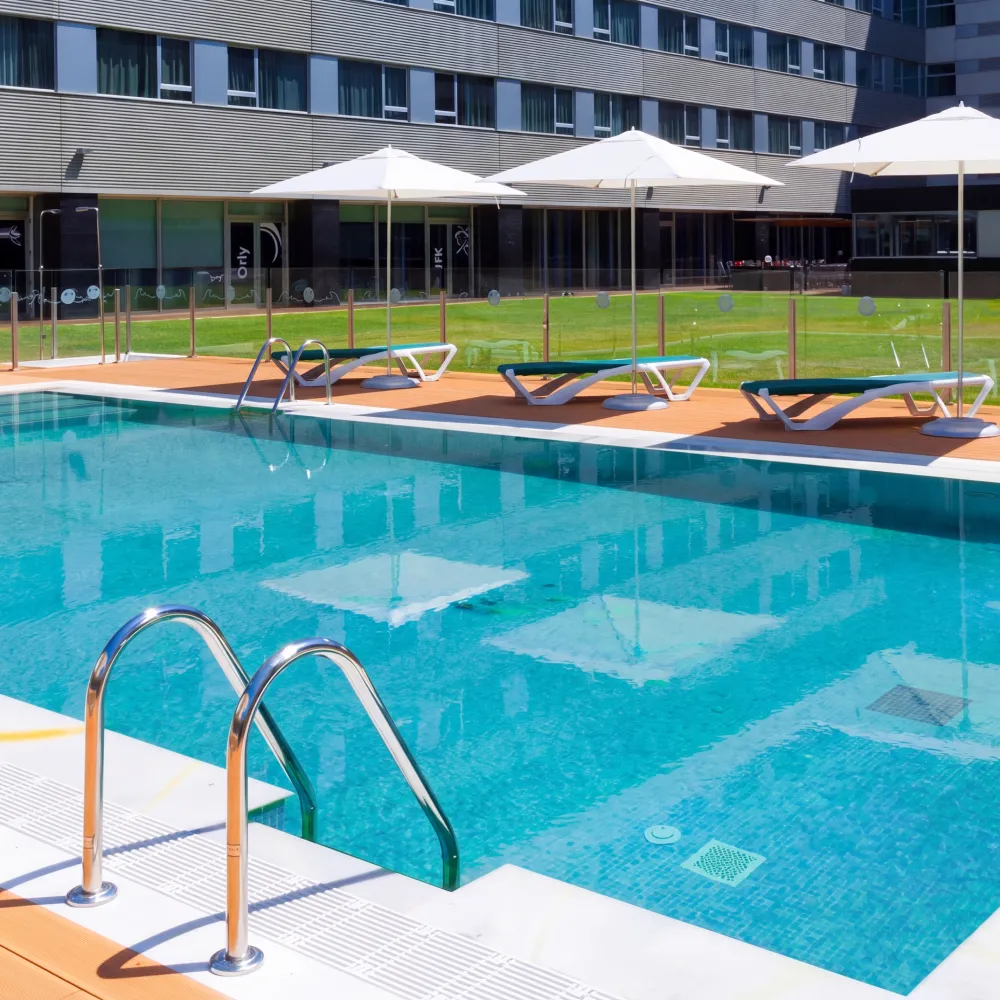 Piscina azul con tumbonas y sombrillas, junto a edificio moderno.