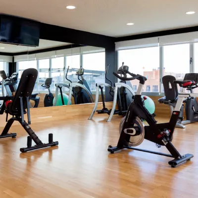Sala de gimnasio con bicicletas est&aacute;ticas y equipo de cardio al sol.