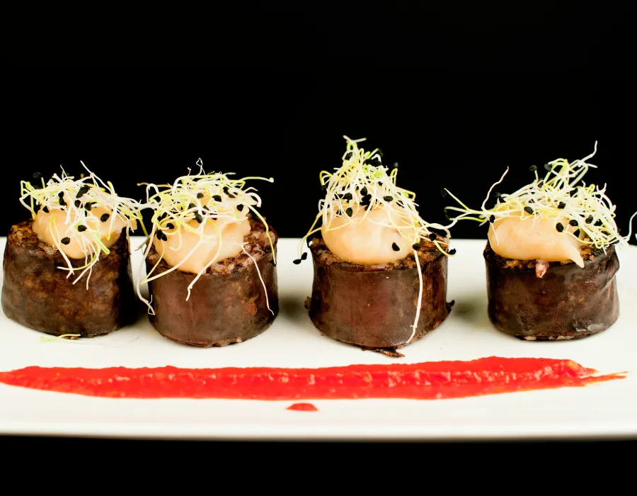 Cuatro piezas de sushi con salsa roja y huevas encima, sobre plato blanco.