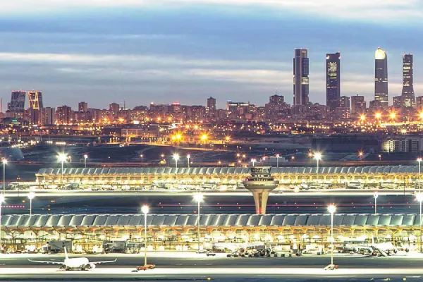 Vista nocturna de un aeropuerto internacional con rascacielos al fondo.