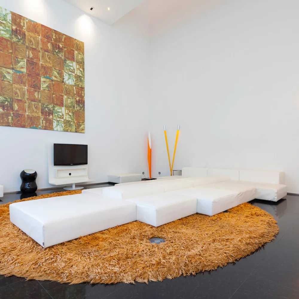 Sala moderna con sof&aacute; blanco en forma de U y alfombra circular marr&oacute;n