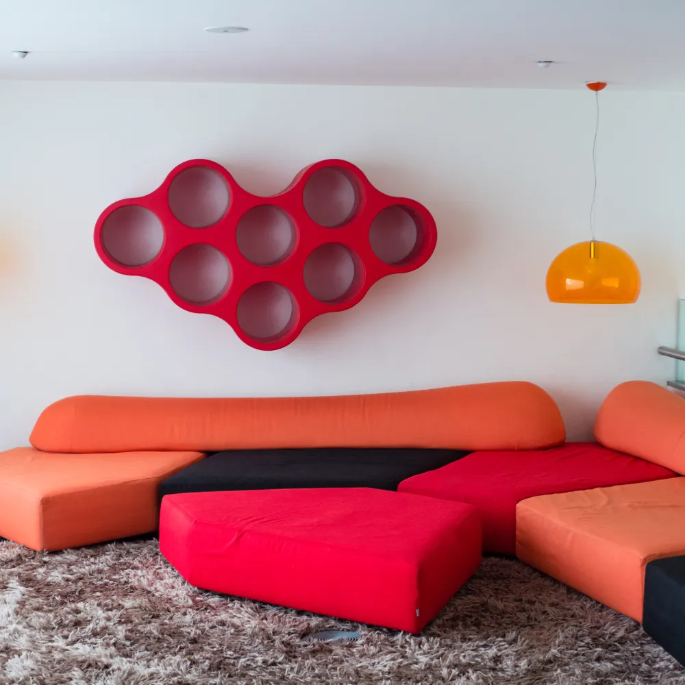 Mural rojo en forma de bota con cojines naranjas y grises en sala infantil