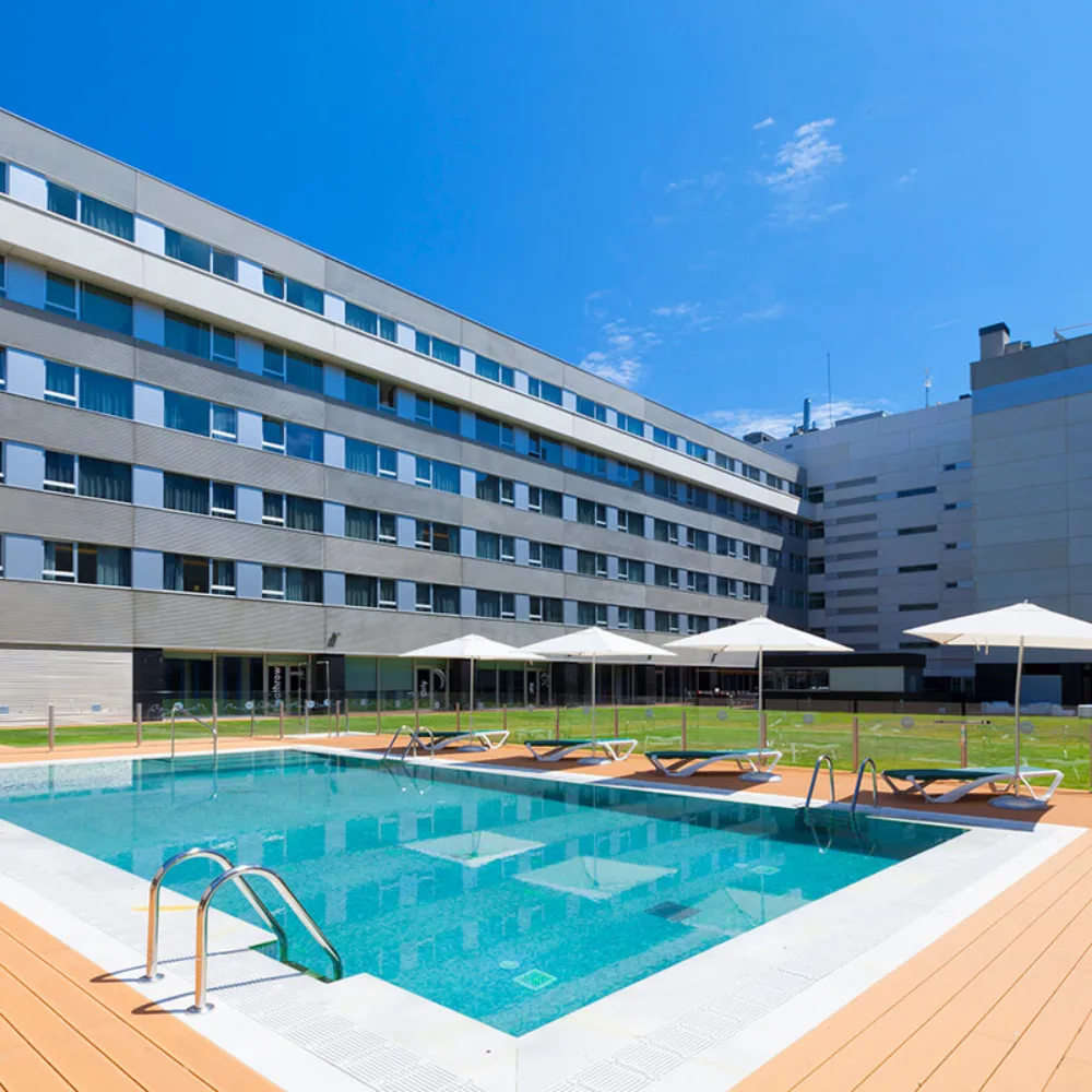Piscina exterior con tumbonas y edificio de apartamentos bajo cielo azul