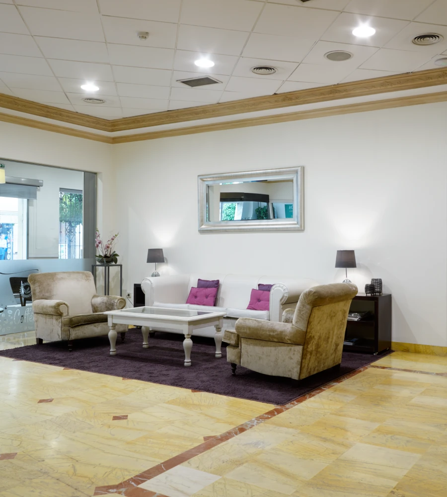 Sala de espera moderna con sillones, l&aacute;mparas y mesa blanca, interior blanco