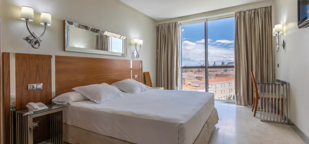 Dormitorio moderno con cama doble, l&aacute;mparas y ventana panor&aacute;mica al cielo