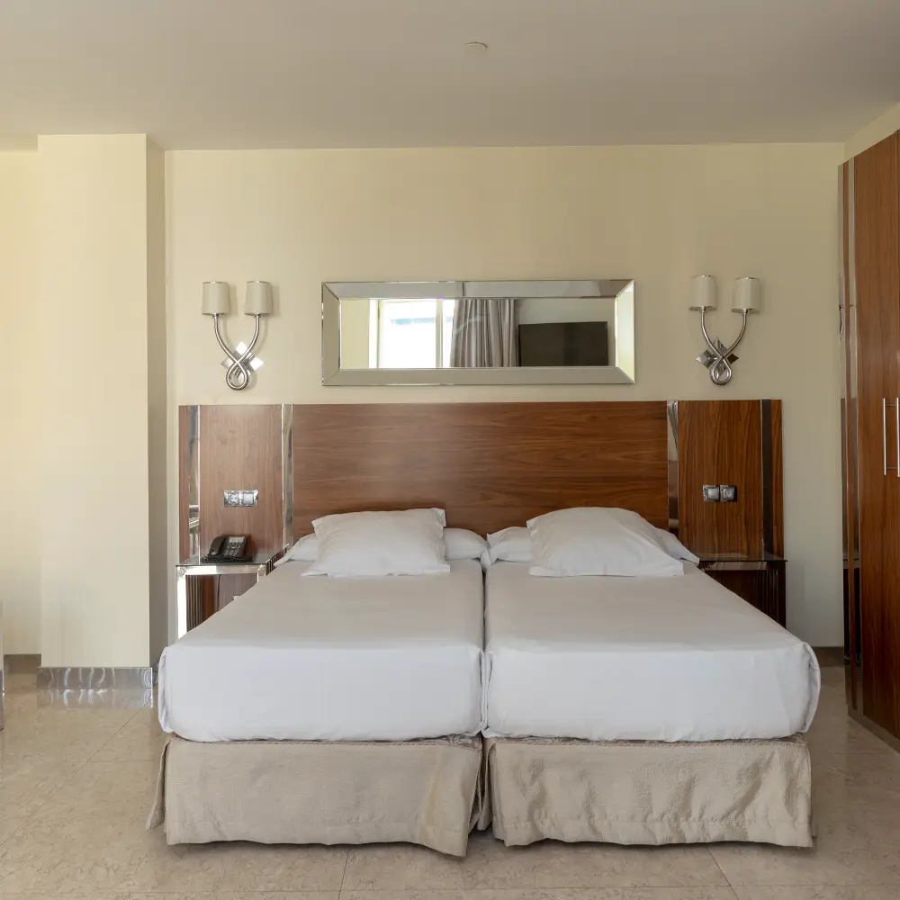 Habitaci&oacute;n moderna con cama doble blanca, espejo y l&aacute;mparas de pared