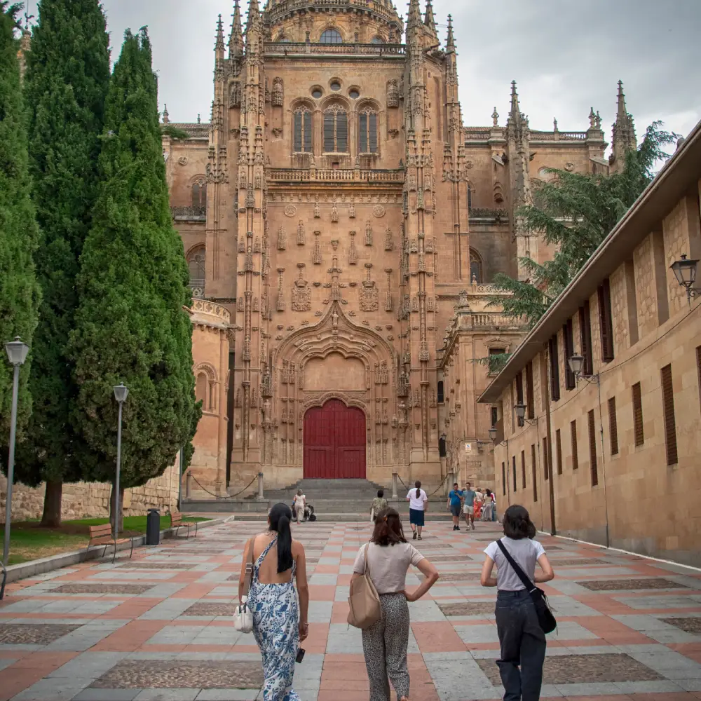 Turistas caminan hacia la fachada g&oacute;tica de una catedral con grandes puertas rojas.