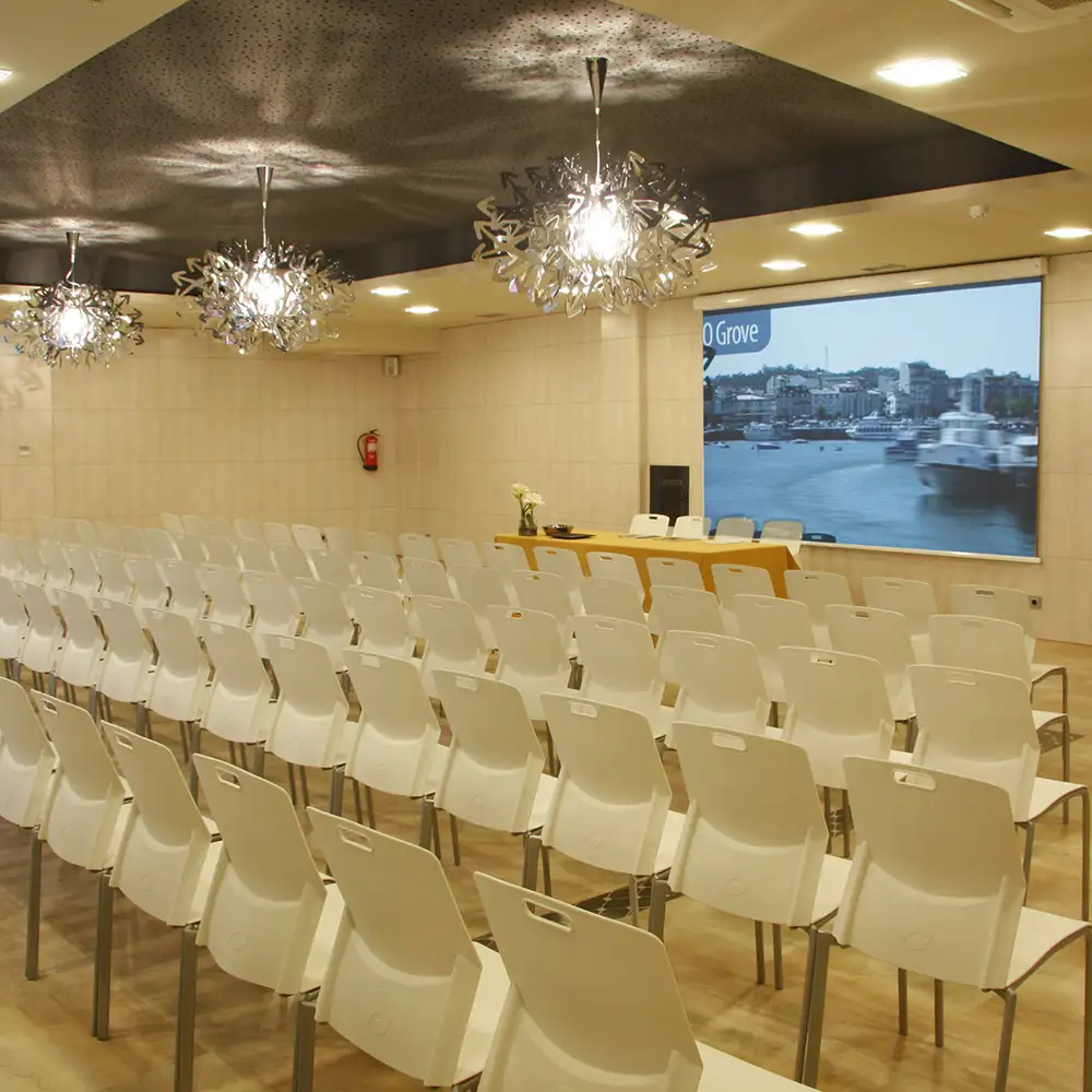 Sala de conferencias con sillas blancas y pantallas con vista al r&iacute;o