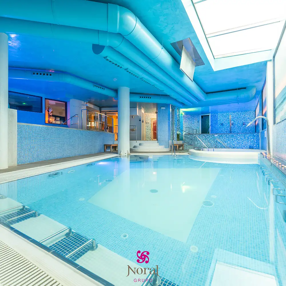 Piscina cubierta moderna con azulejos y luces azules, interior de spa