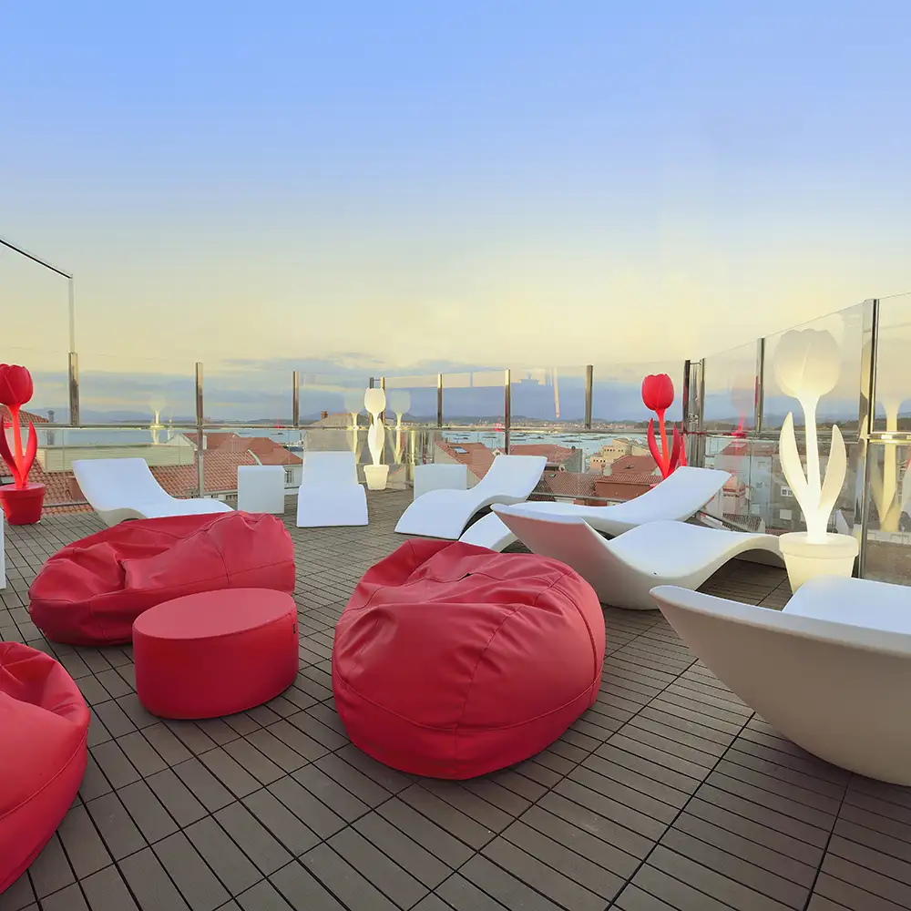 Terraza con sillones y muebles blancos y rojos frente al mar al atardecer