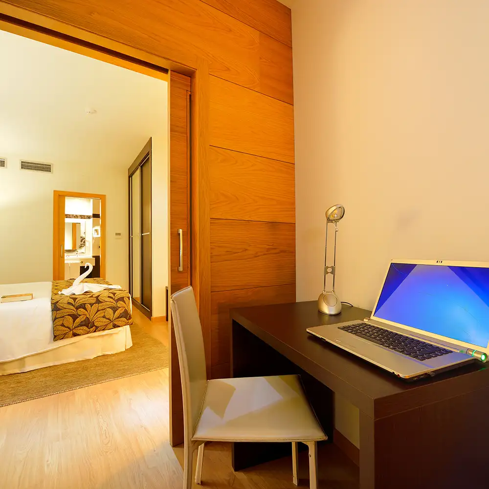 Escritorio con laptop y l&aacute;mpara, puerta de madera y cama en habitaci&oacute;n hotel