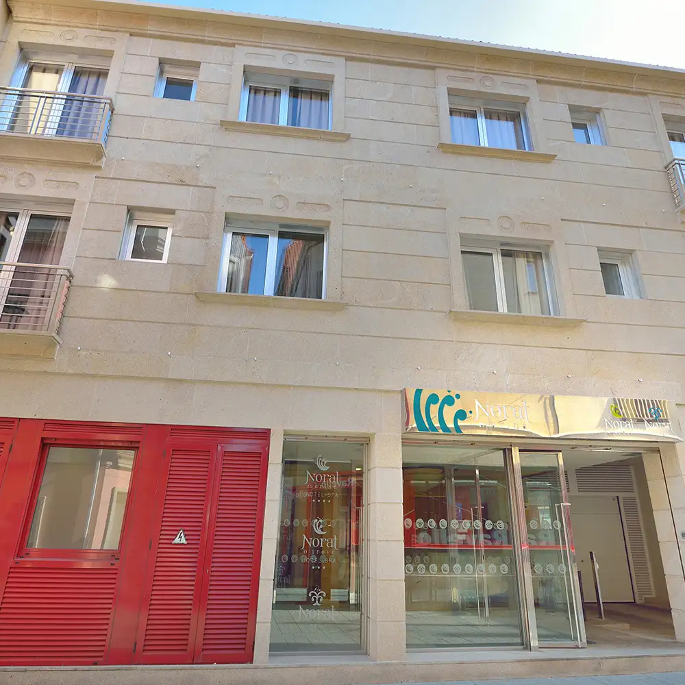 Fachada de edificio de piedra con puertas rojas y ventanales, a cielo abierto