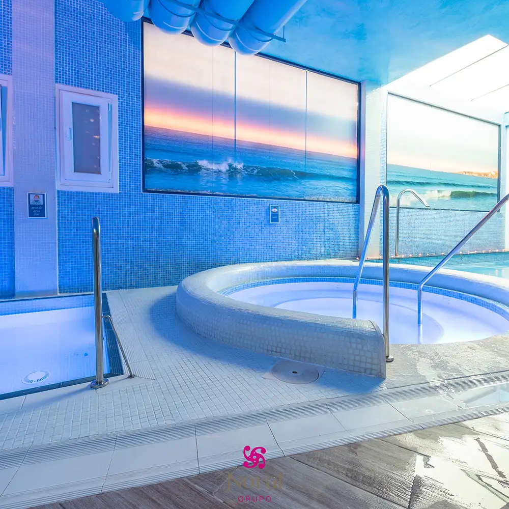 Jacuzzi interior con azulejos azules y vistas al mar al atardecer